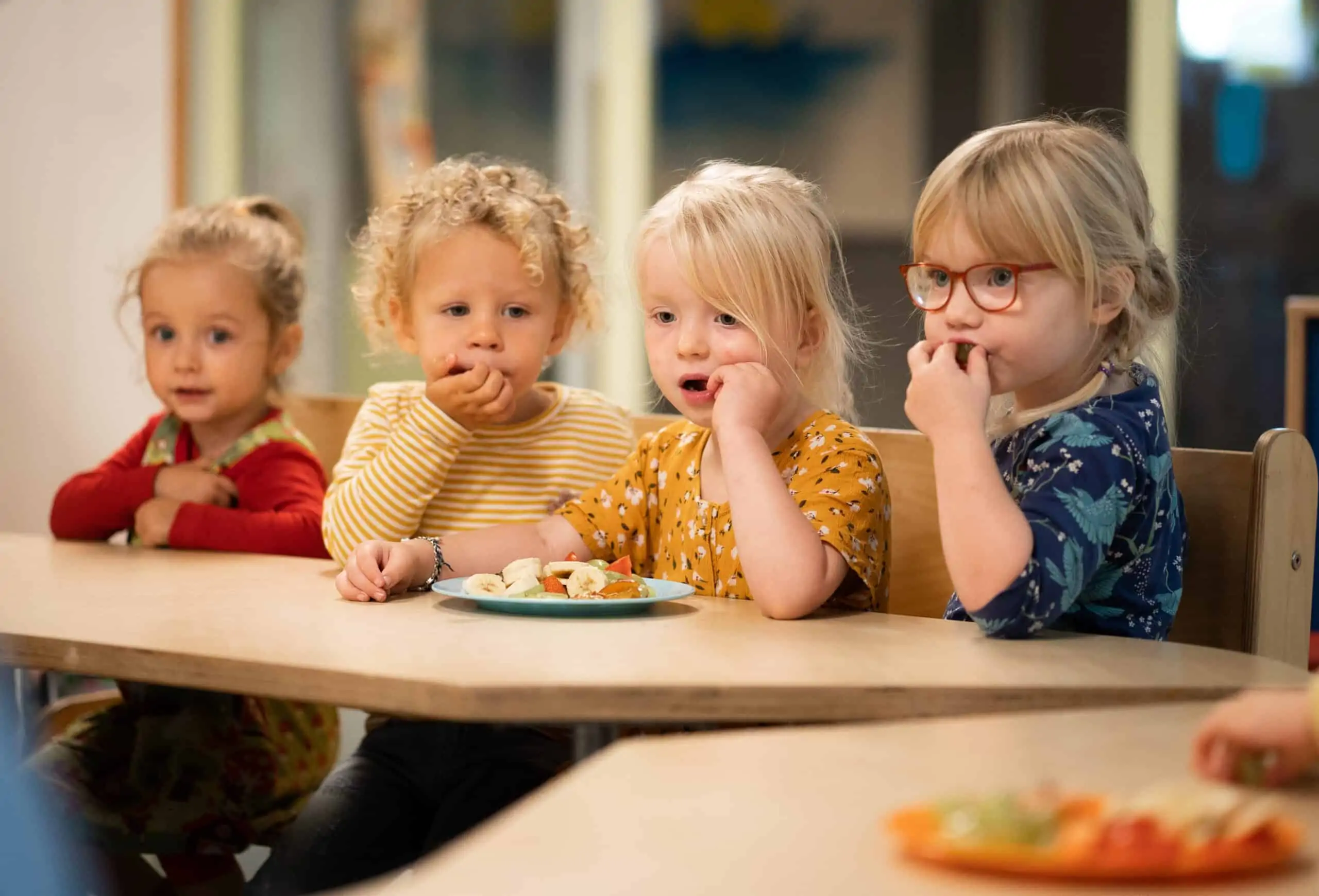 Vier peuters eten samen fruit aan tafel bij Poespas
