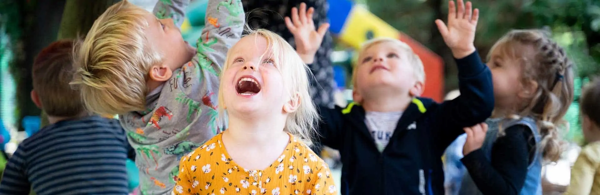 Vier kinderen kijken lachend omhoog in de tuin van Poespas